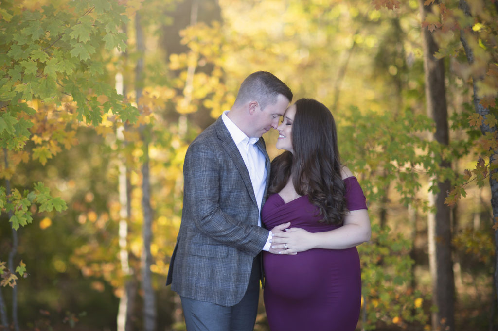 Husband and wife standing close to each other touching noses while each has one hand on mom's pregnant belly. Rates page placeholder.