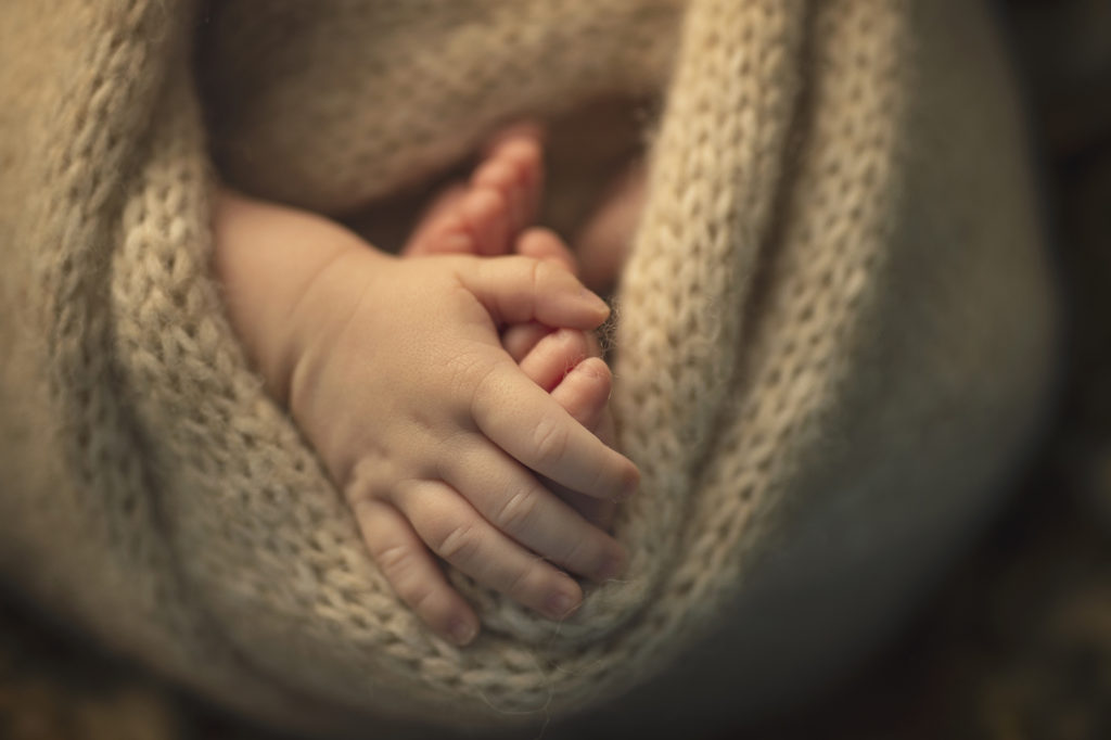 Macro photo of a newborn hand holding their own foot wrapped up in a fluffy knit wrap. Printed products page place holder.