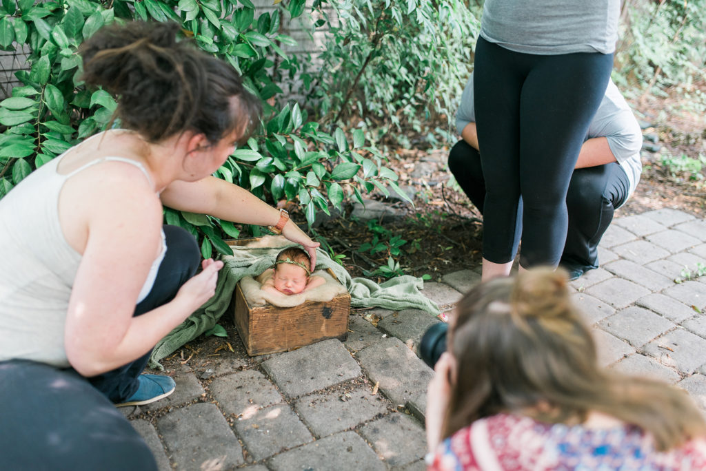 Female newborn photographer mentoring others by showing them how to pose a baby safely in a prop.